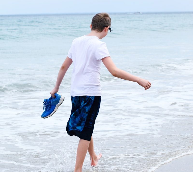 boy in white t-shirt and blue shorts running on beach during daytime