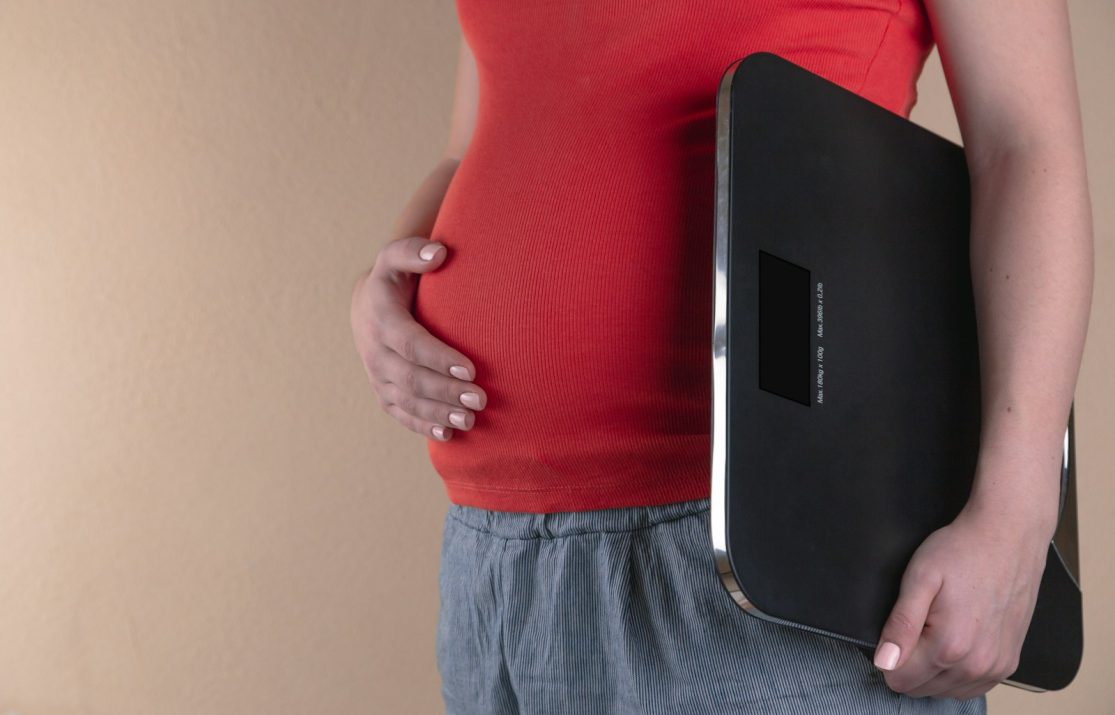 pregnant woman touching her belly and carrying a digital bathrooms cale